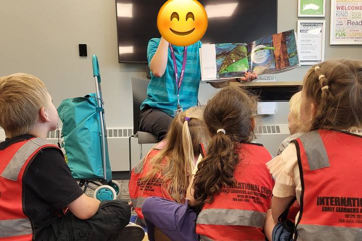 School-age children in safety vests listening to an educator read a story