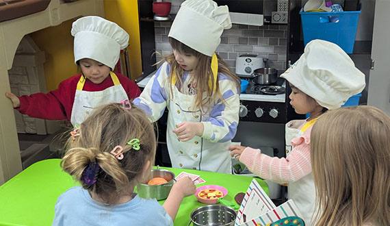 Preschoolers in chef hats playing in a toy kitchen