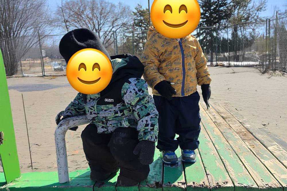 Two young children in snowsuits on the outdoor play area