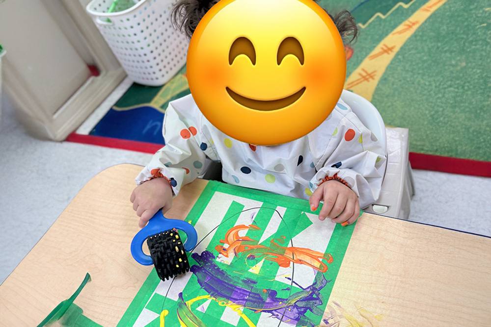 Baby painting with a toy wheel at a table