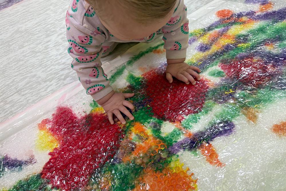 Baby exploring colourful paint under a plastic sheet