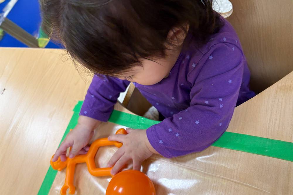 Baby playing with orange toys on a high-chair tray