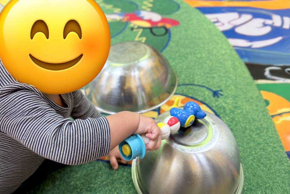 Baby exploring metal bowls and toy cars on the rug