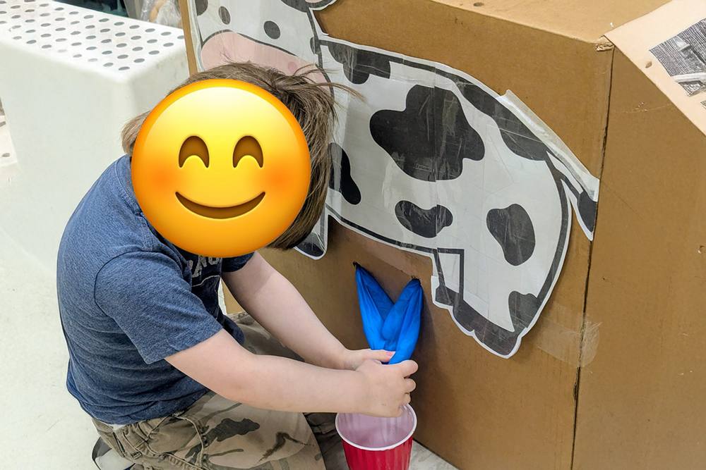 Preschooler milking a pretend cardboard cow