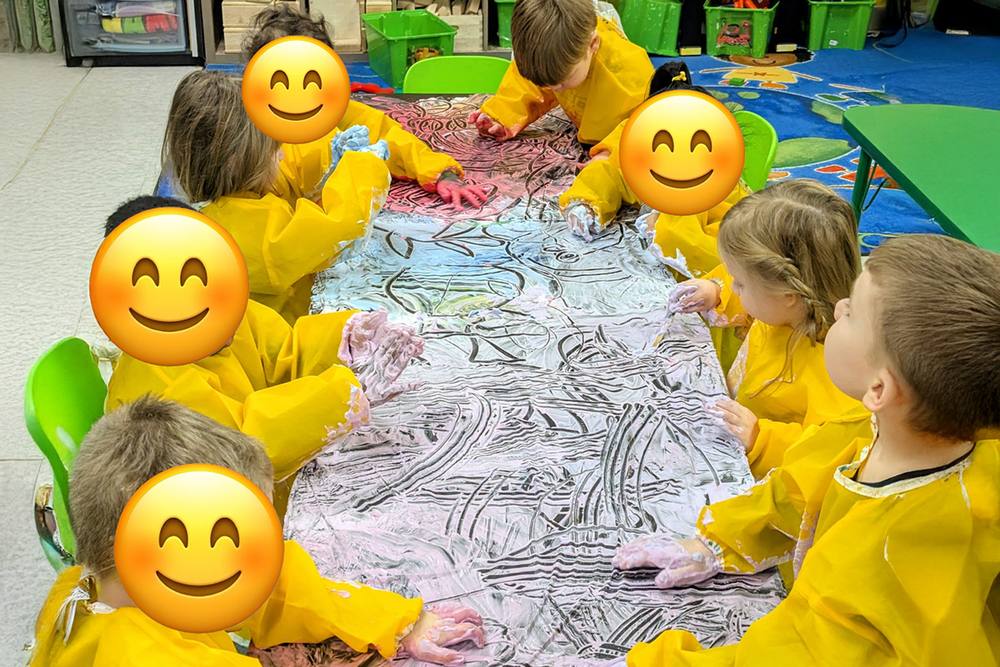 Preschoolers in smocks painting a long paper mural