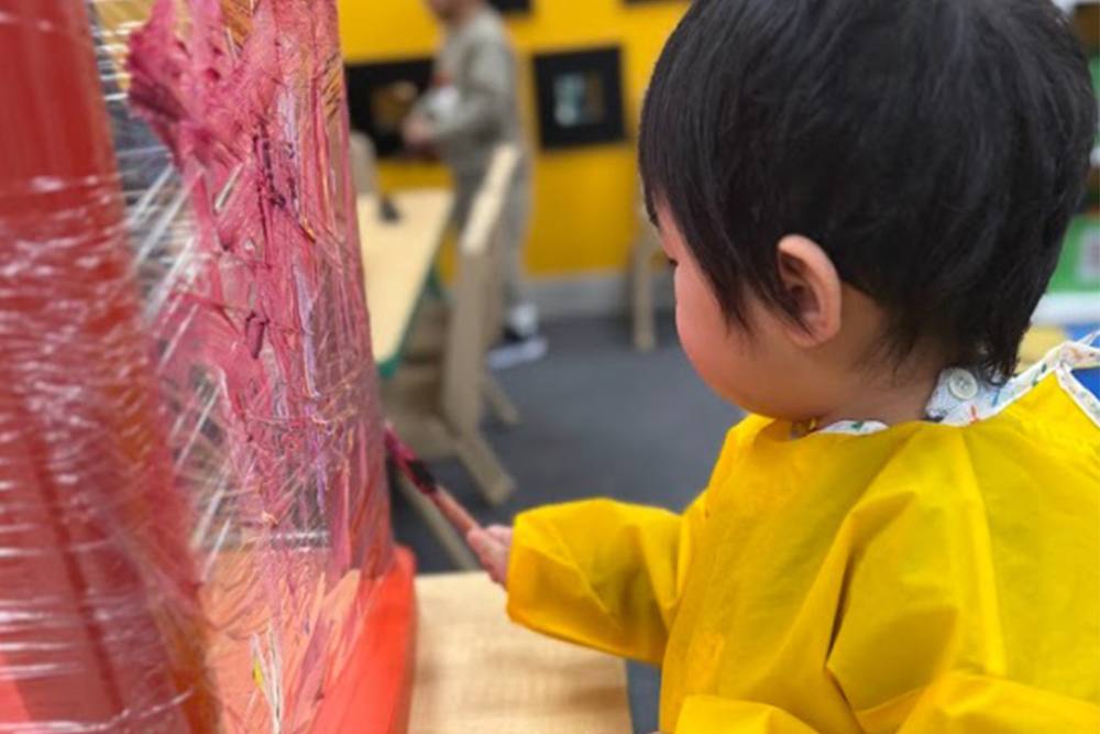 Toddler painting on a plastic-wrap wall