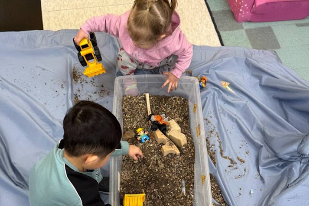 Toddlers digging in a sensory bin with toy excavators