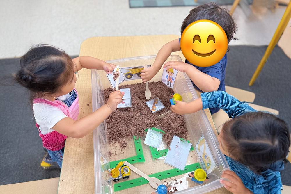 Toddlers exploring a sensory bin with toy vehicles