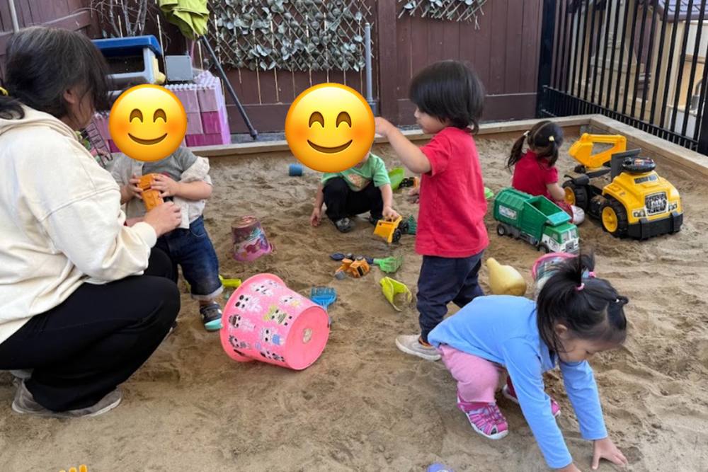 Toddlers digging in the outdoor sandbox with an educator