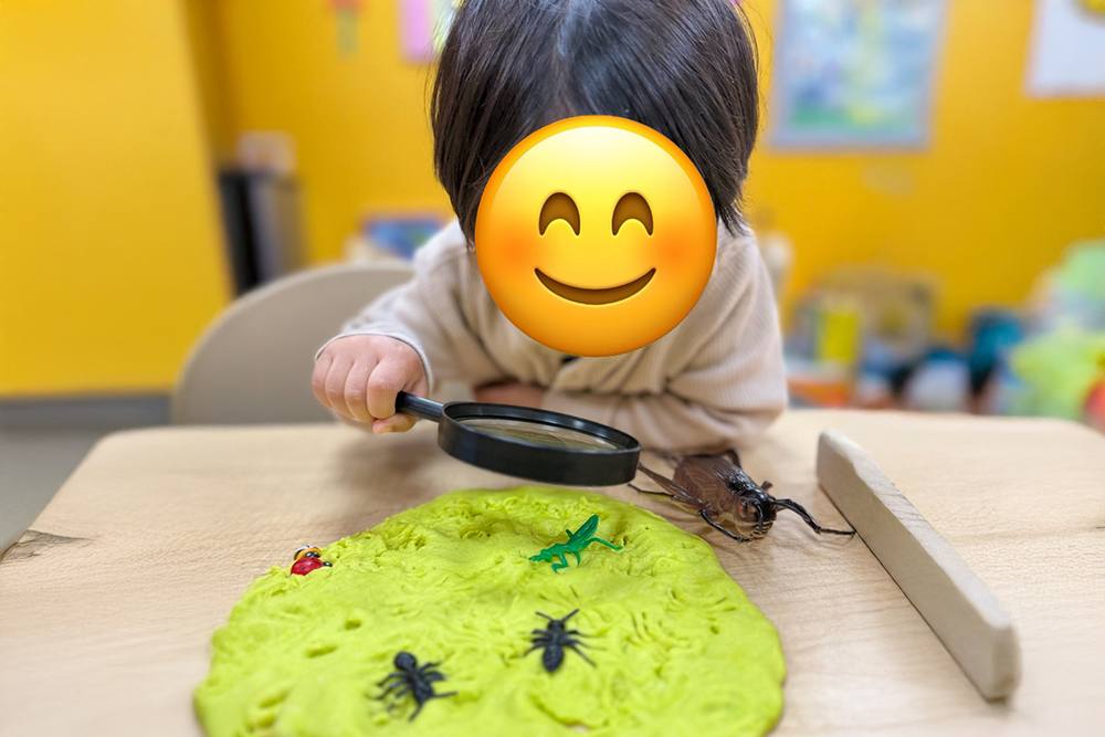 Toddler using a magnifying glass to look at toy bugs in play dough