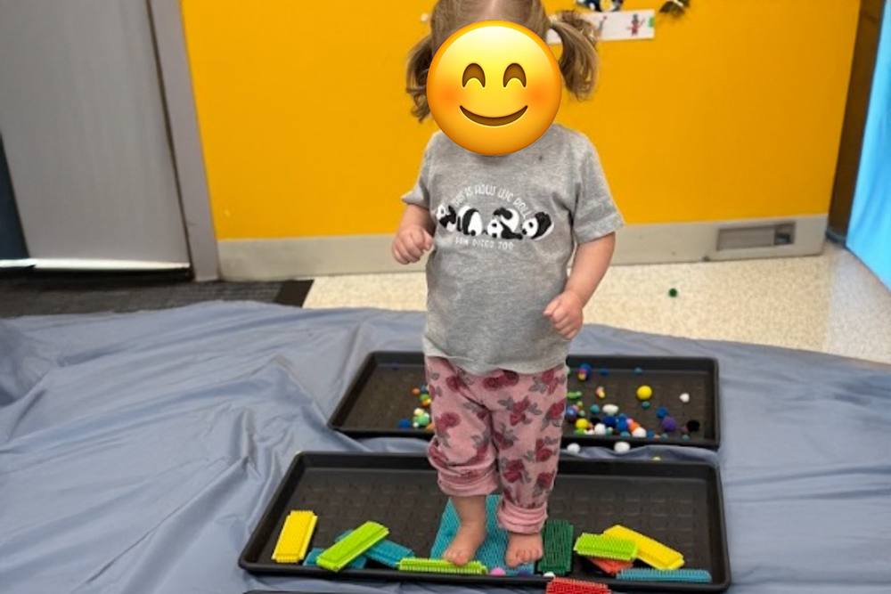 Toddler standing on a sensory path of textured trays